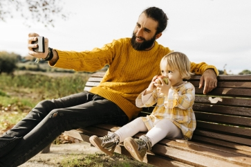 man taking selfie on bench with small girl